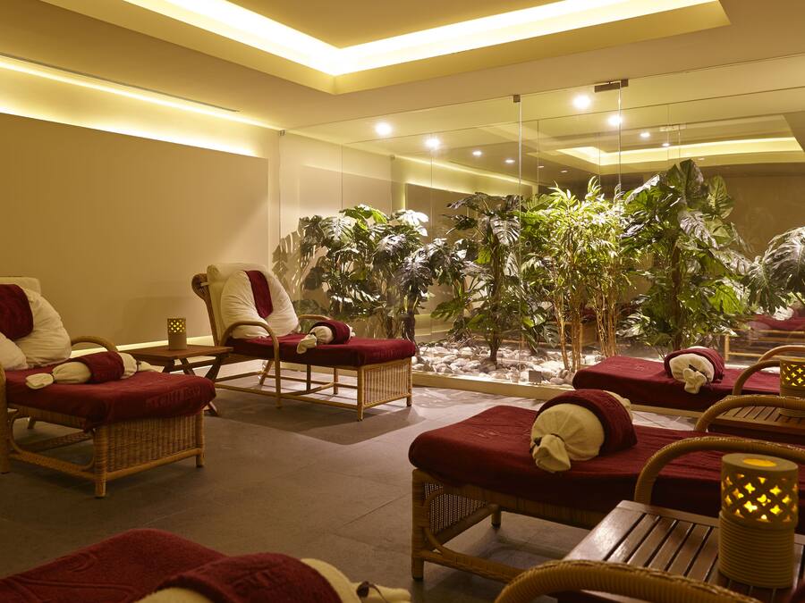 Un área de spa con sillones de mimbre, cojines rojos y un amplio arreglo de plantas de interior.