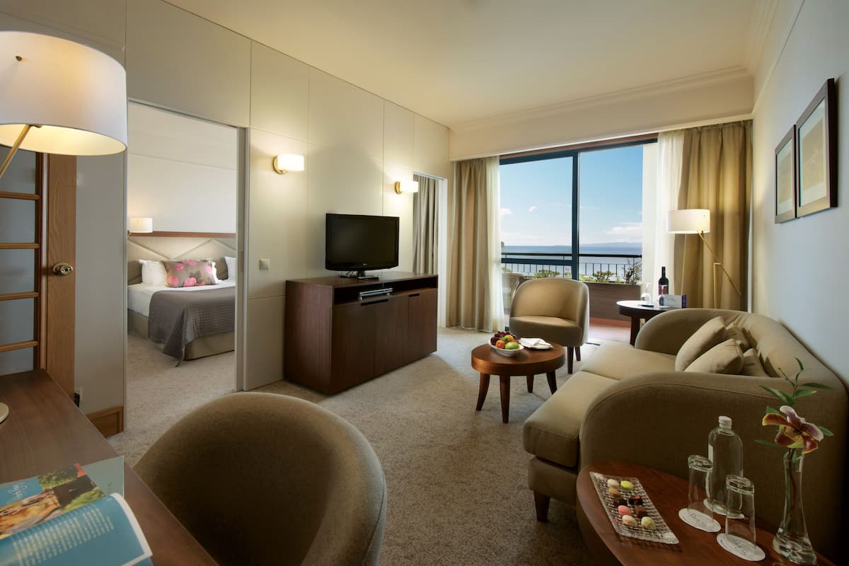 Habitación de hotel con cama, televisor, sofá, mesa de centro y balcón con vistas.