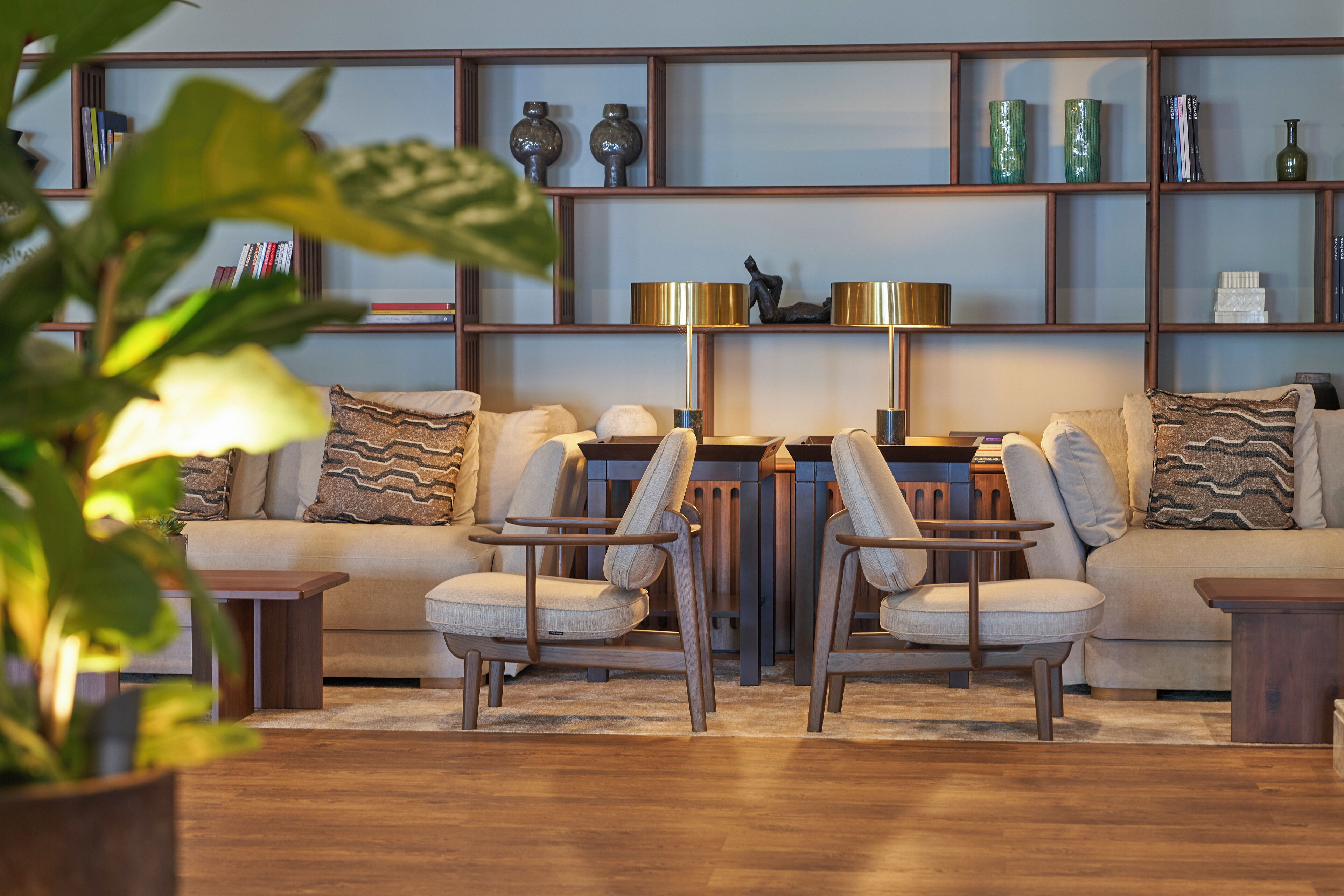Een woonkamer met een bank, twee fauteuils, een salontafel en een boekenkast vol decoratieve objecten.