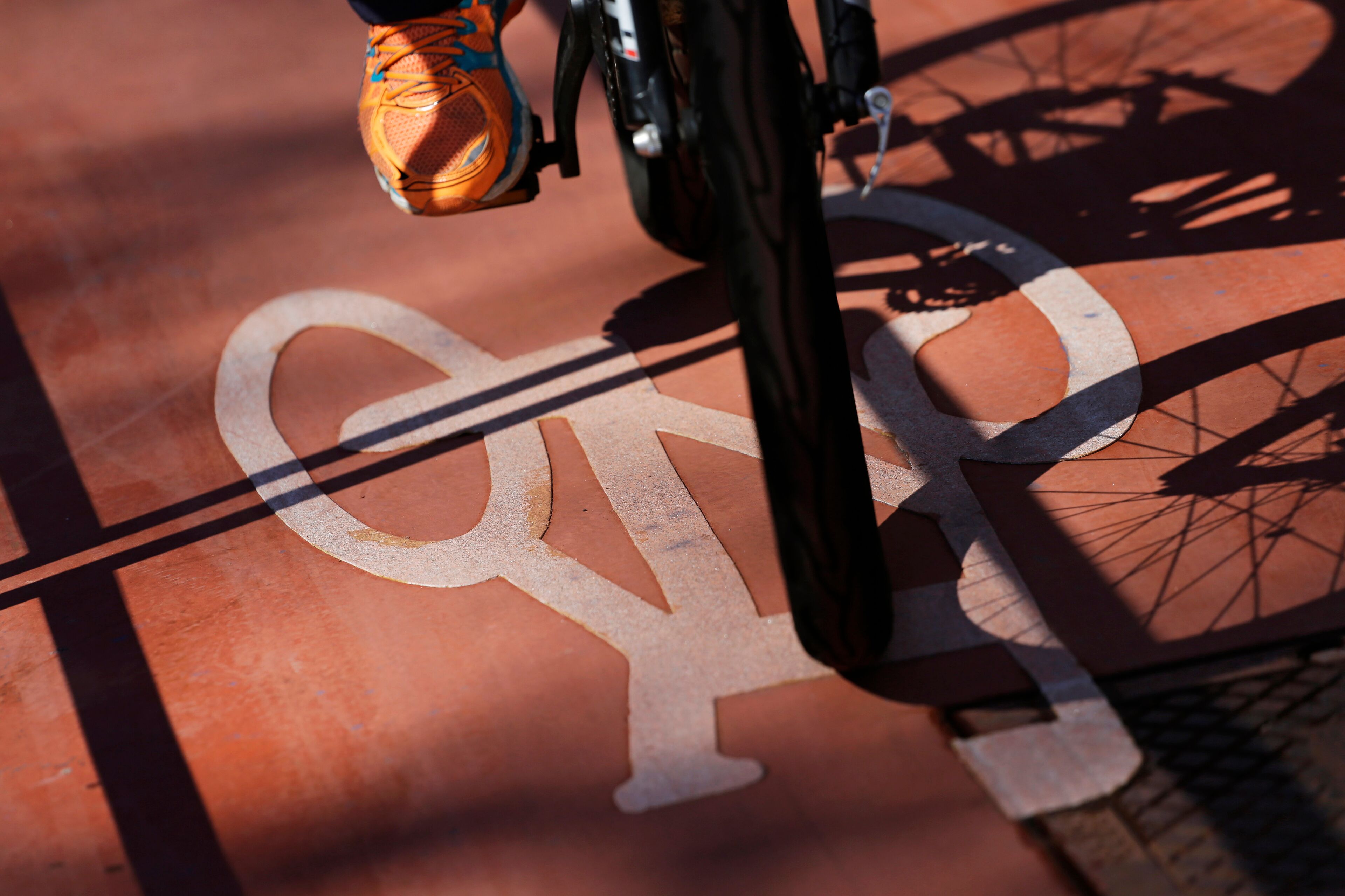 A bicycle with a white frame and orange details, positioned over a red surface with a white bicycle symbol.