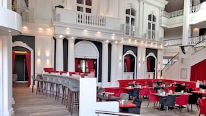 A spacious restaurant with high ceilings, red and black chairs, and a bar area. - DORMERO Hotel Stuttgart (Stuttgart)
