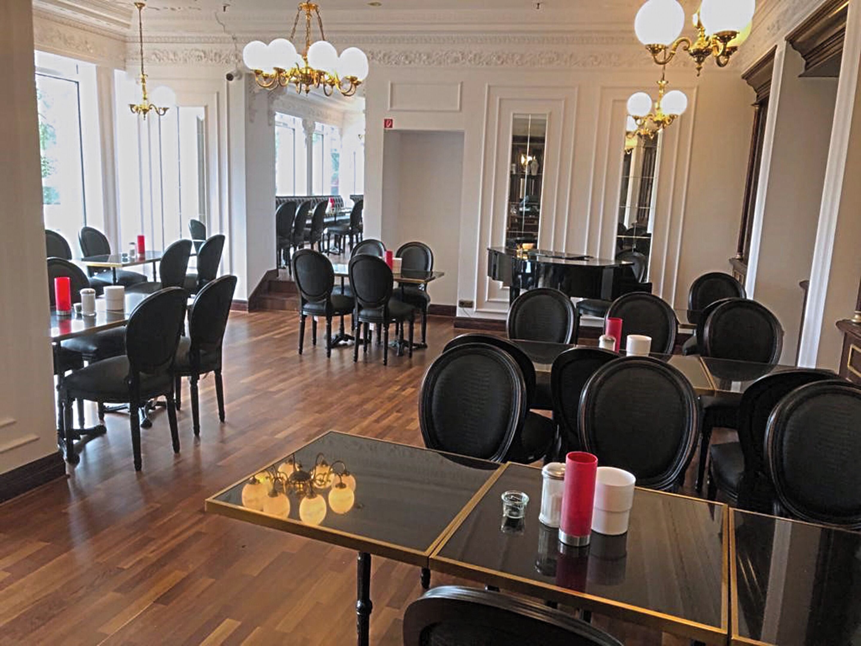 A dining area with multiple tables and chairs, chandeliers, and a piano in the background.
