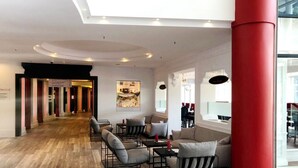 A spacious lobby with a wooden floor, a red column, and a seating area with sofas and tables. - DORMERO Hotel Stuttgart (Stuttgart)