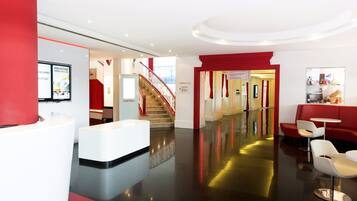 Een hotel lobby met een receptiebalie, een trap en zithoeken.