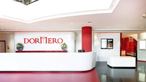 A modern hotel reception area with a prominent 'DORMERO' sign, a red accent wall, and a clean, reflective floor. - DORMERO Hotel Stuttgart (Stuttgart)