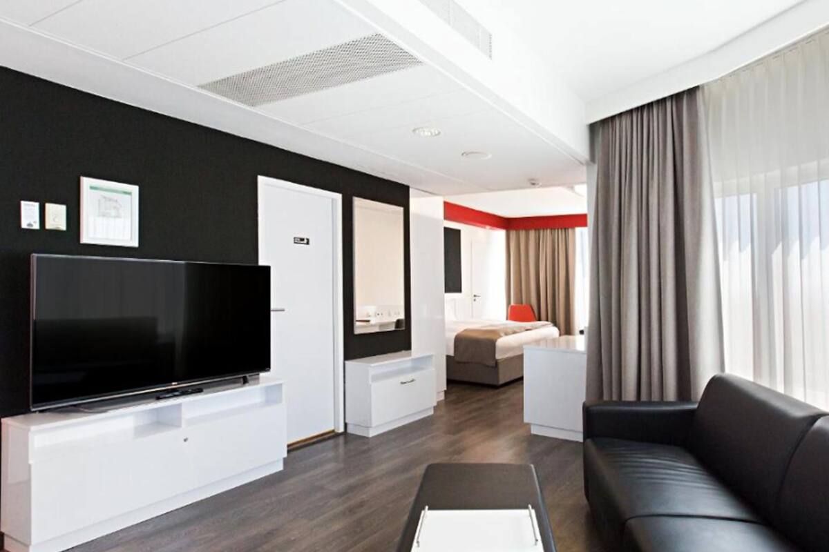A modern hotel room with a flat-screen TV, a sofa, a desk, and a bed.