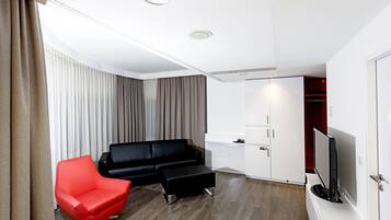 Ein modernes Wohnzimmer mit einem schwarzen Sofa, einem roten Sessel, einem schwarzen Hocker, einem Flachbildfernseher und einer weißen Kommode.