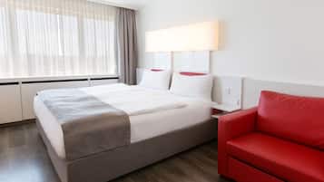 Ein Hotelzimmer mit einem Bett, einem roten Sofa, einem großen Fenster mit durchsichtigen Vorhängen und einer Wandlampe.