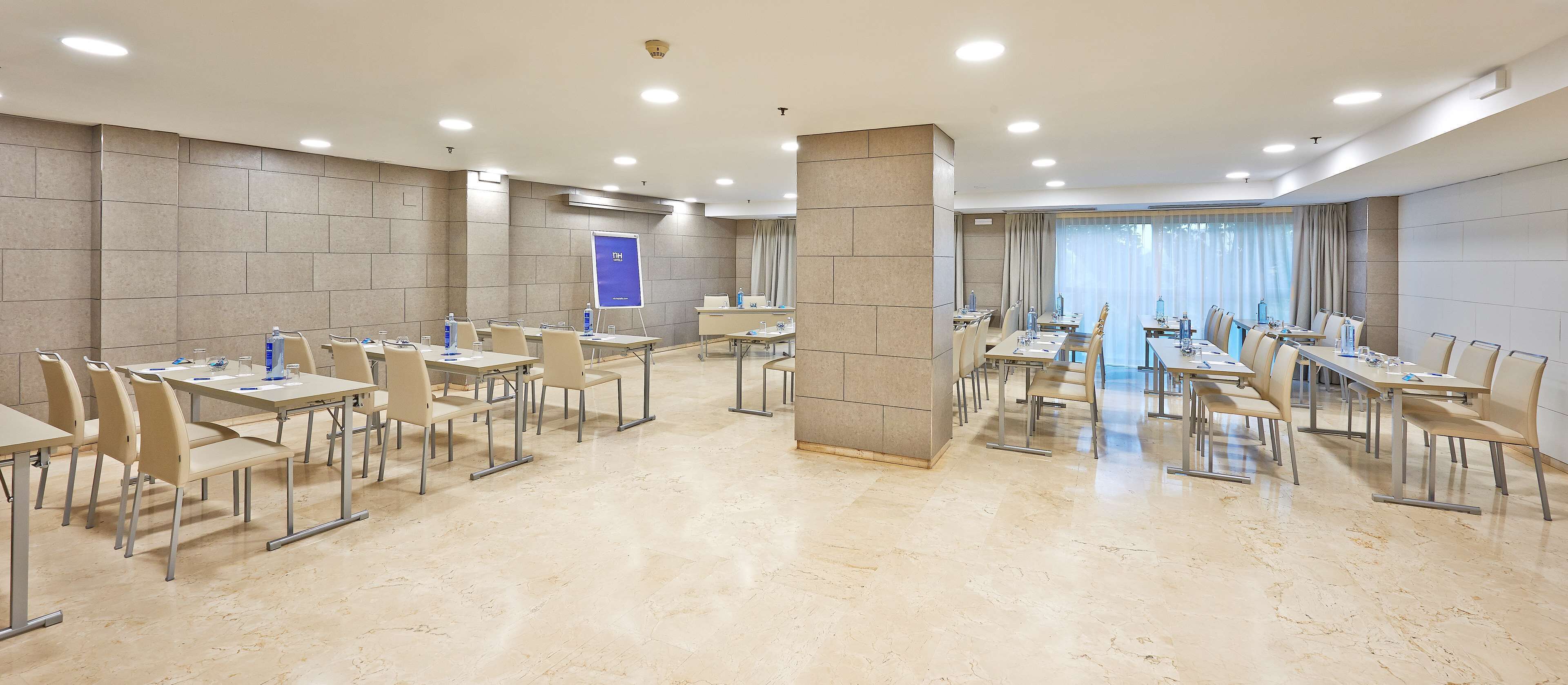 Un salón de conferencias con varias mesas y sillas, una pizarra y un amplio ventanal con cortinas.