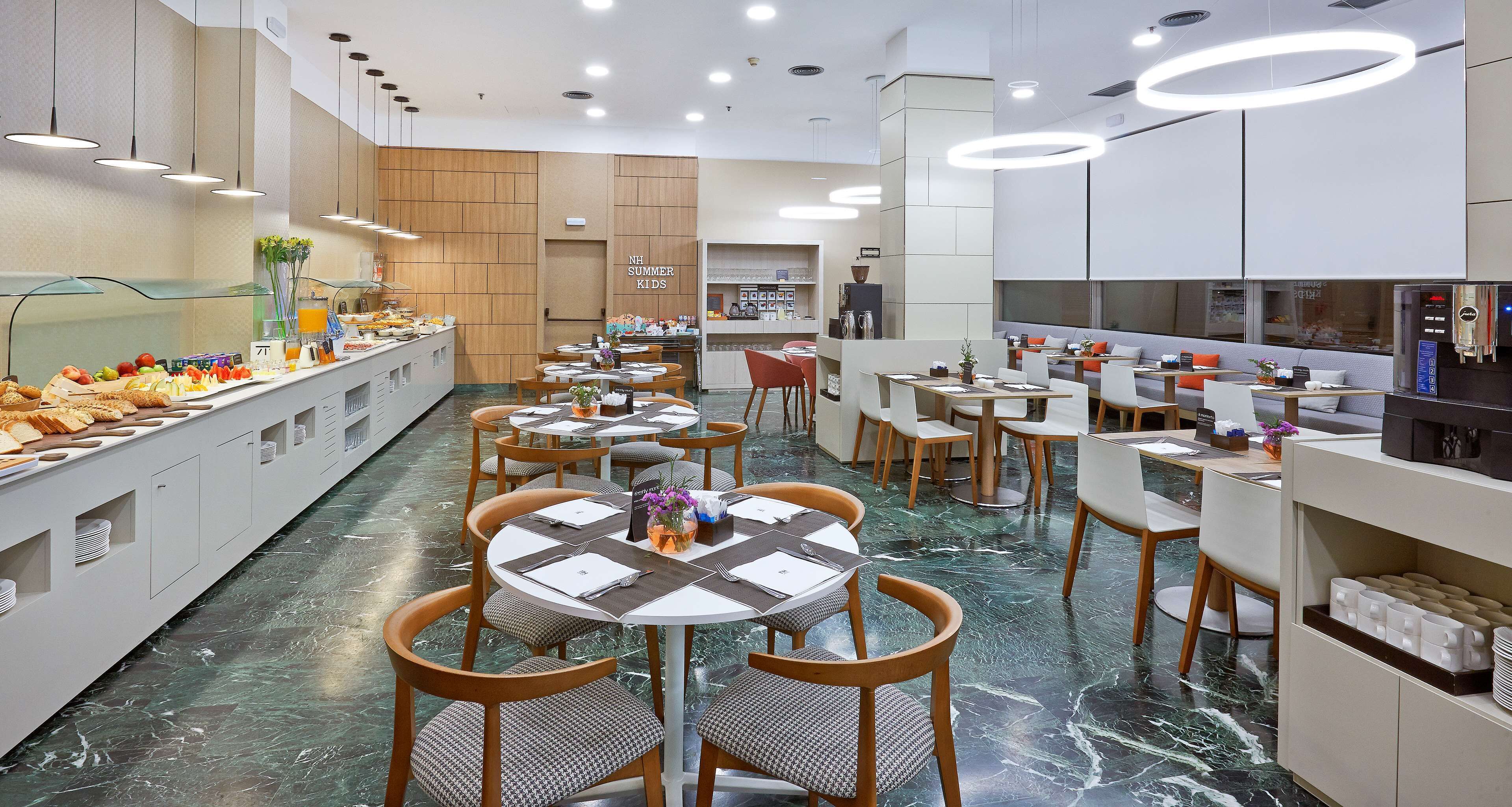Un comedor moderno con mesas y sillas redondas, un bufé a la izquierda y una zona de cocina a la derecha.
