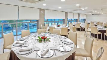 A banquet hall with round tables set for dining, large windows offering a view of a bridge and greenery, and a modern interior design.