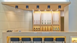 Una zona de bar con mostrador, taburetes y estanterías llenas de botellas de licores.