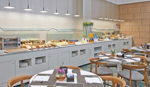 A buffet setup with a variety of food items, a coffee machine, and a seating area with tables and chairs. - NH Ciudad de Zaragoza (Zaragoza)