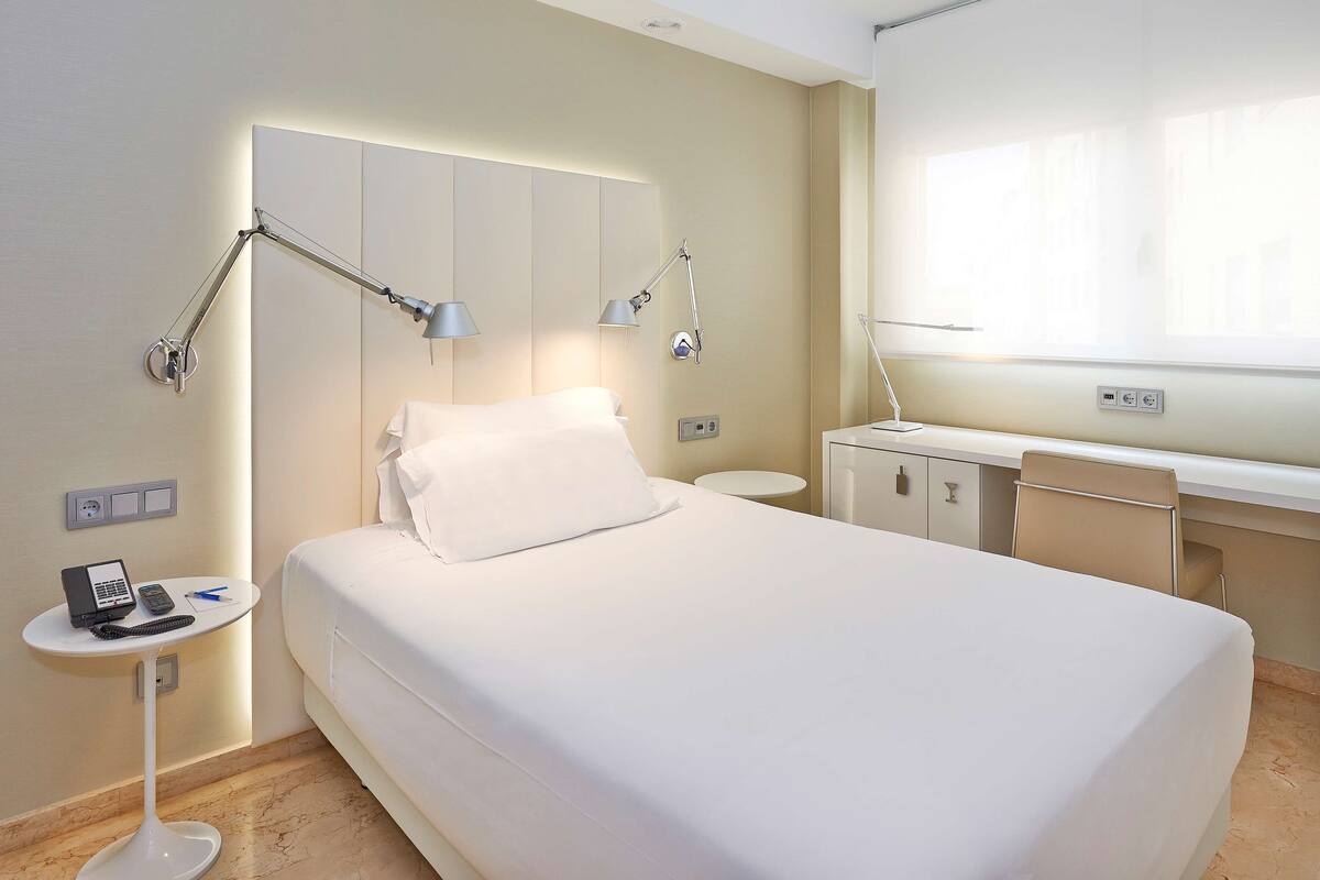 Une chambre d’hôtel avec un lit, une table de chevet, un bureau et une fenêtre.