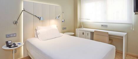 A hotel room with a bed, bedside table, desk, and a window.
