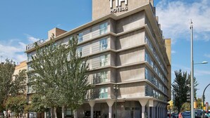 Un moderno edificio de hotel con un llamativo letrero 'nh hotels', varios pisos y una zona de entrada cubierta.