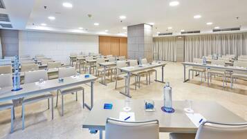 Una sala de conferencias con varias mesas y sillas, equipada con botellas de agua y tarjetas de identificación.