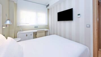 Une chambre d’hôtel équipée d’un lit, d’un bureau, d’une chaise, d’un téléviseur fixé au mur et d’une fenêtre.