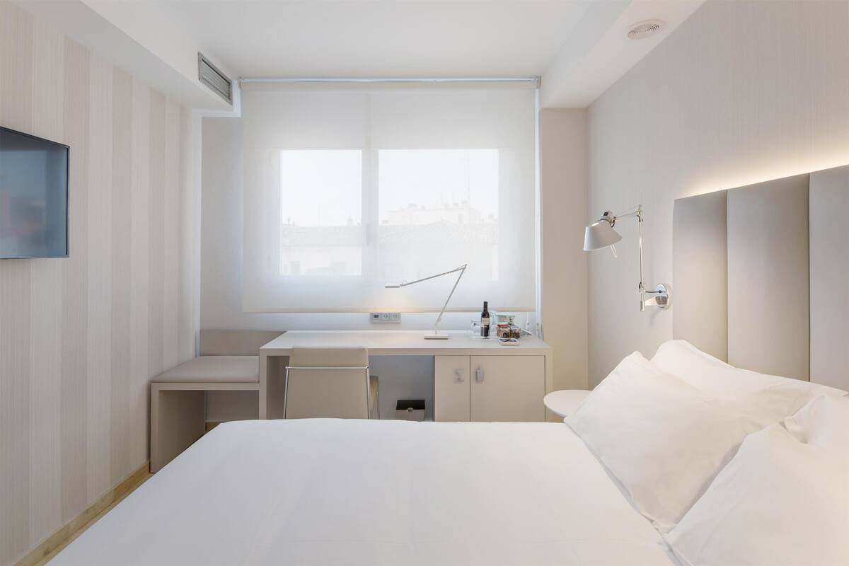 Une chambre d’hôtel moderne équipée d’un lit, d’un bureau, d’une chaise, d’une fenêtre et d’une table de chevet.