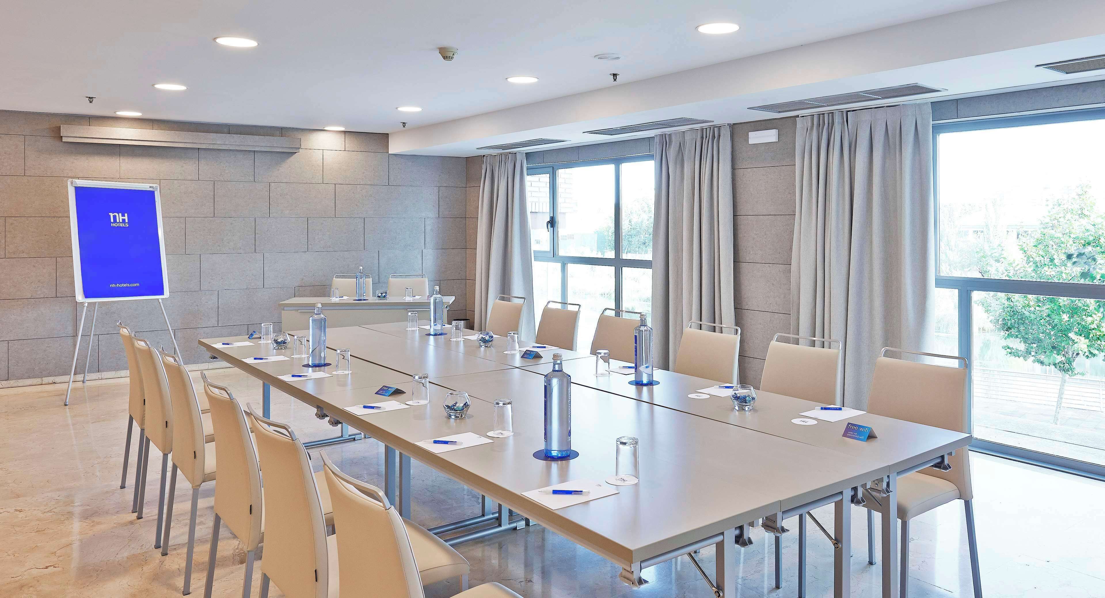 A conference room with a long table, chairs, a whiteboard, and a window with curtains.
