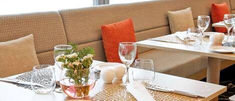 A dining area with a sofa, tables set with cutlery, plates, glasses, and a vase with flowers.
