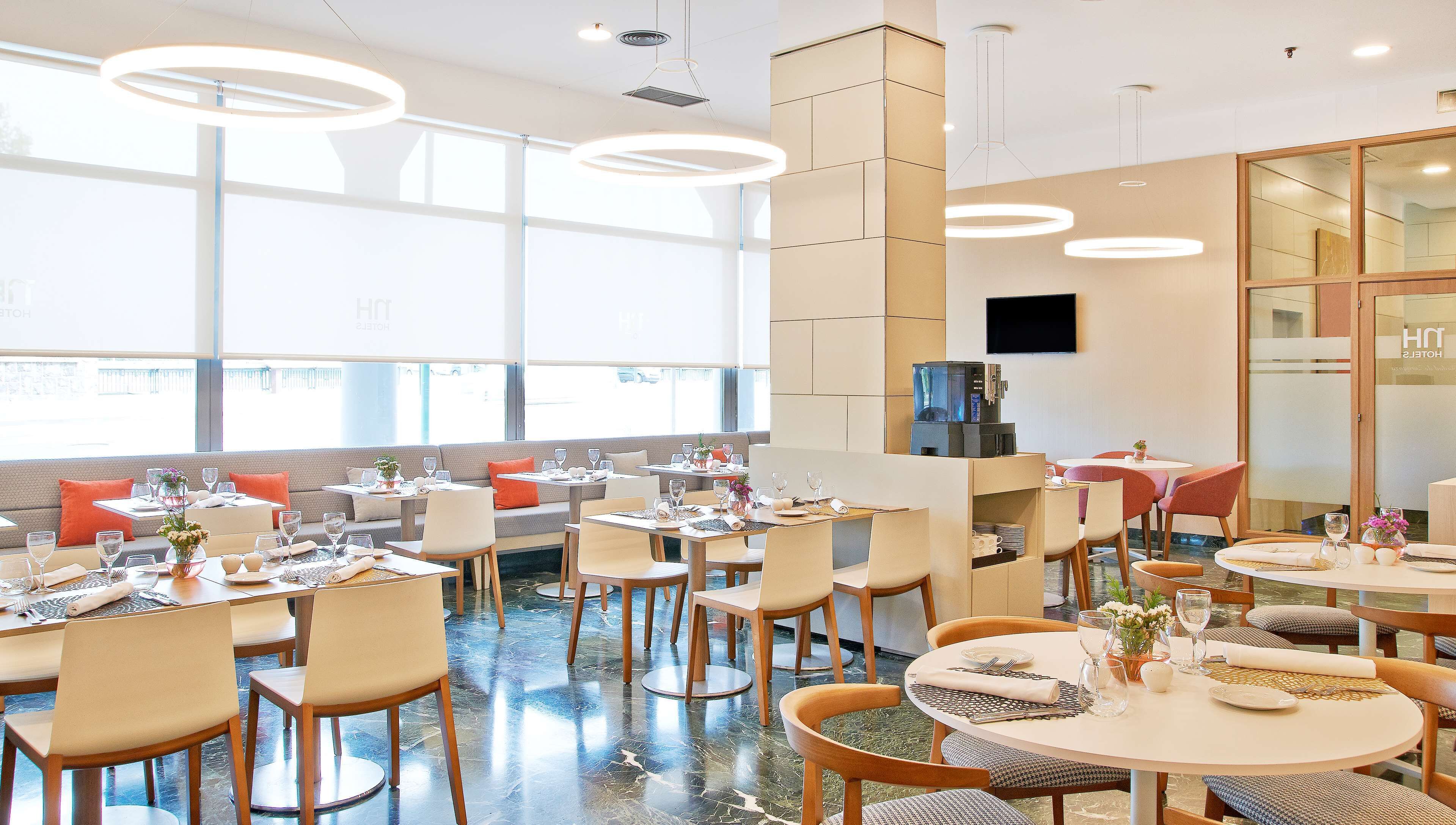 Un comedor moderno de hotel con mesas redondas, asientos cómodos y una máquina de café.