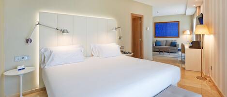 A hotel room with a large bed, bedside lamps, a small table, and a sofa in the background.