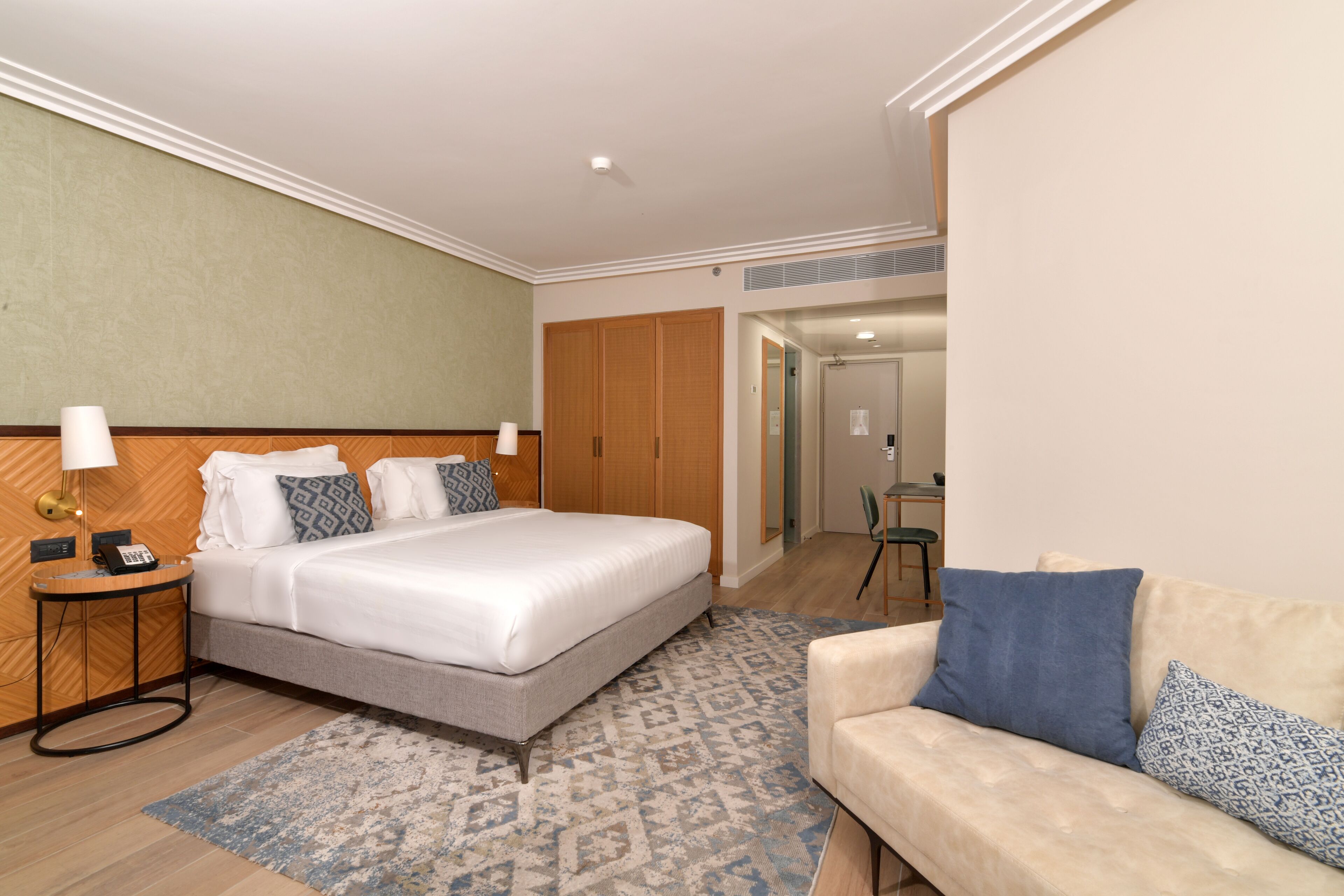 Una habitación de hotel con cama, mesita de noche, lámpara y un sofá.