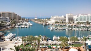 A marina with numerous boats docked, a large hotel building, and a clear blue sky.