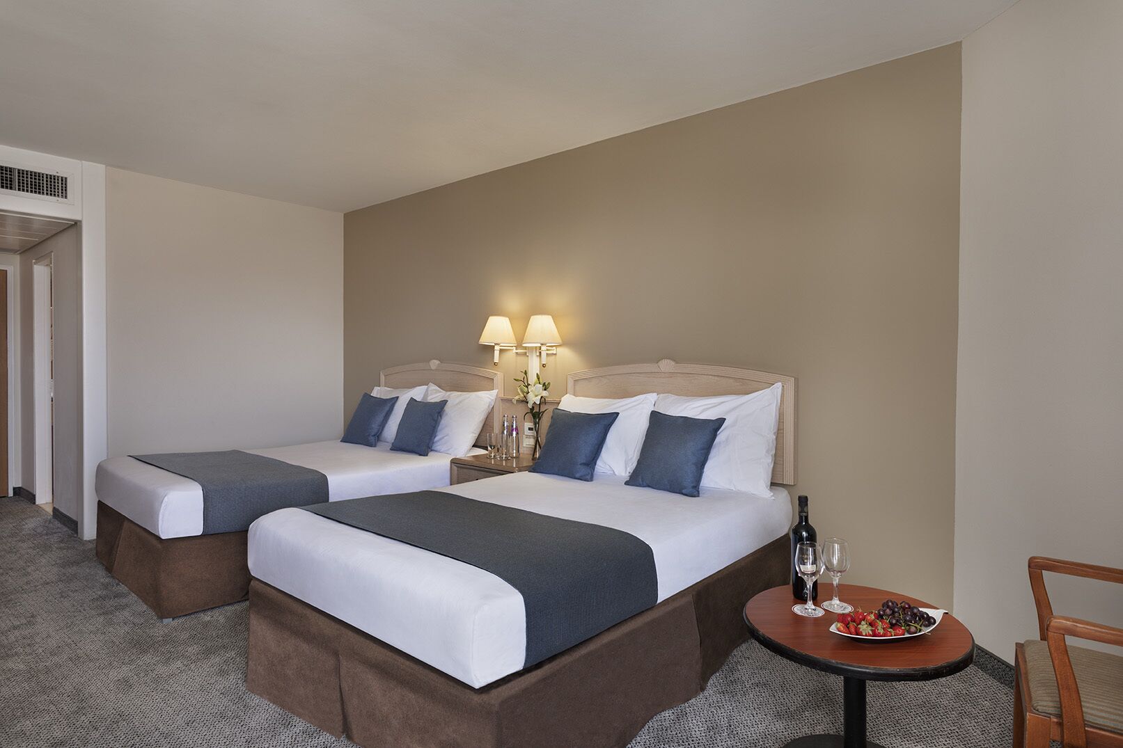 Une chambre d’hôtel avec deux lits, une petite table sur laquelle se trouvent une bouteille et des verres, et une chaise.