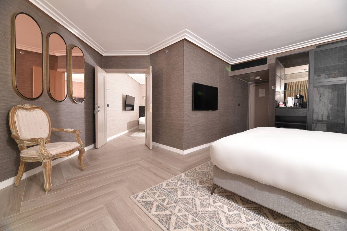 Ein modernes Hotelzimmer mit einem großen Bett, einer Sitzecke mit einem Sessel, einem Fernseher und einem Spiegel.