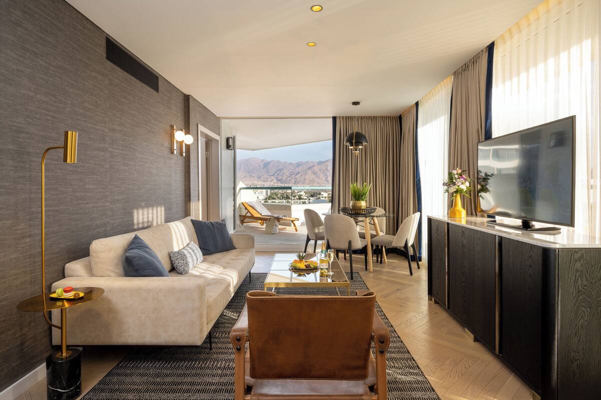 Ein modernes Hotelzimmer mit Sofa, Sessel, Essbereich und Fernseher.