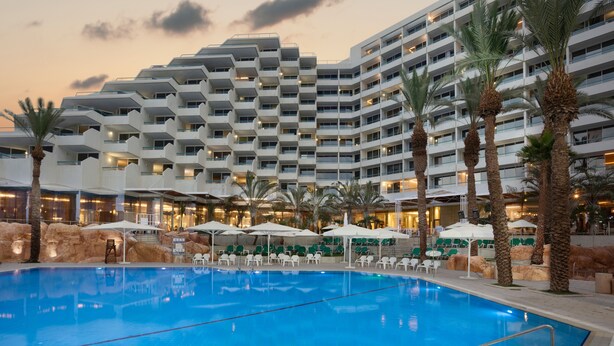 A hotel with a large indoor swimming pool, multiple balconies, and outdoor seating areas with umbrellas.