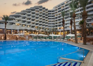 A hotel with a large indoor swimming pool, multiple balconies, and outdoor seating areas with umbrellas.