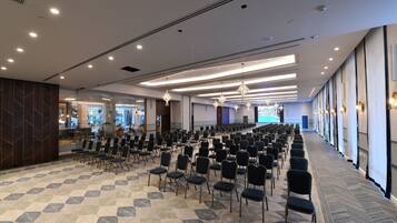 Un salón de conferencias con filas de sillas, una alfombra estampada y luminarias modernas.