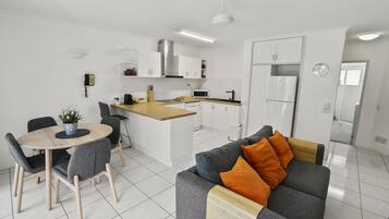 A modern kitchen with white cabinets, a central island, and a dining area with a round table and chairs.