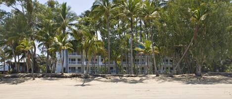 A beachfront hotel with multiple-story buildings, palm trees, and a sandy beach.