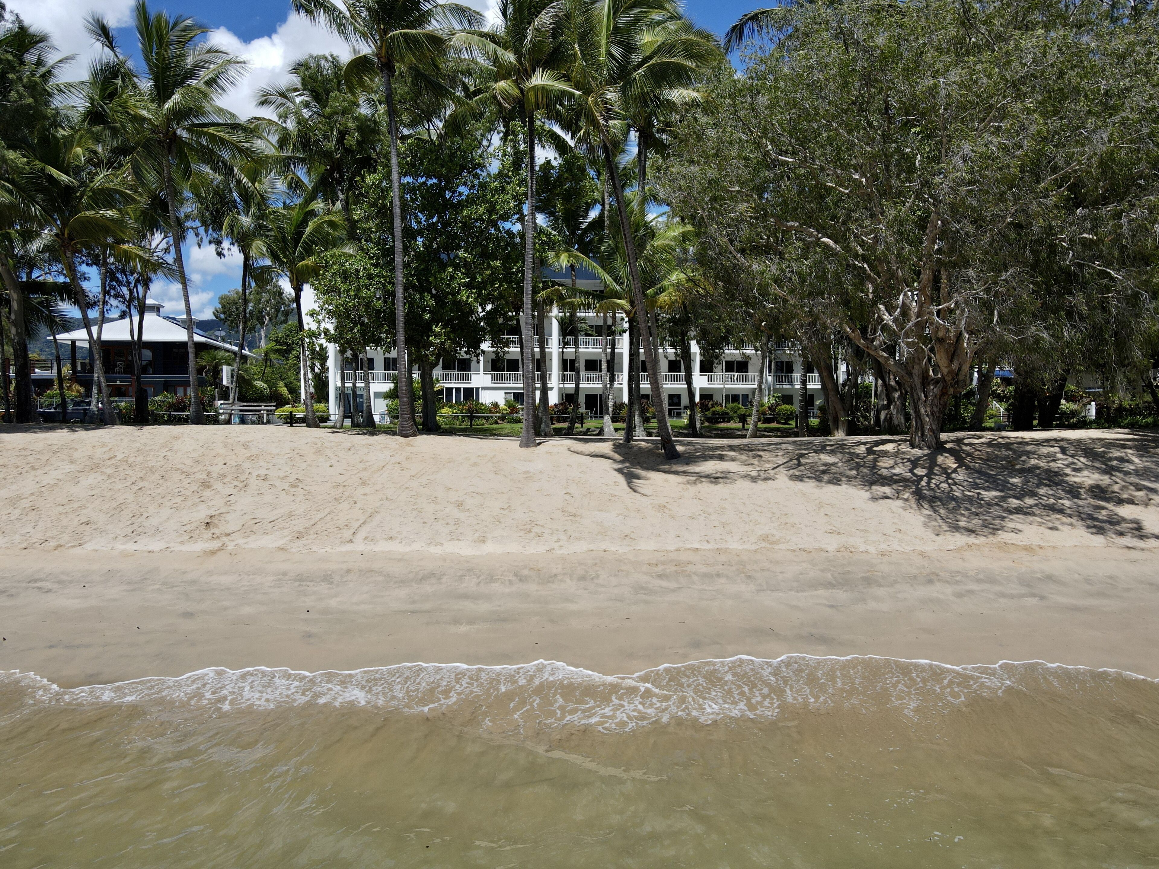 A beachfront hotel with multiple-story buildings, palm trees, and a sandy beach.