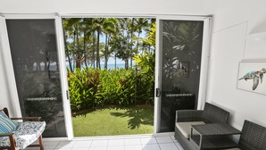 Una habitación moderna con puerta corrediza de vidrio que da a un jardín tropical y vistas al océano.