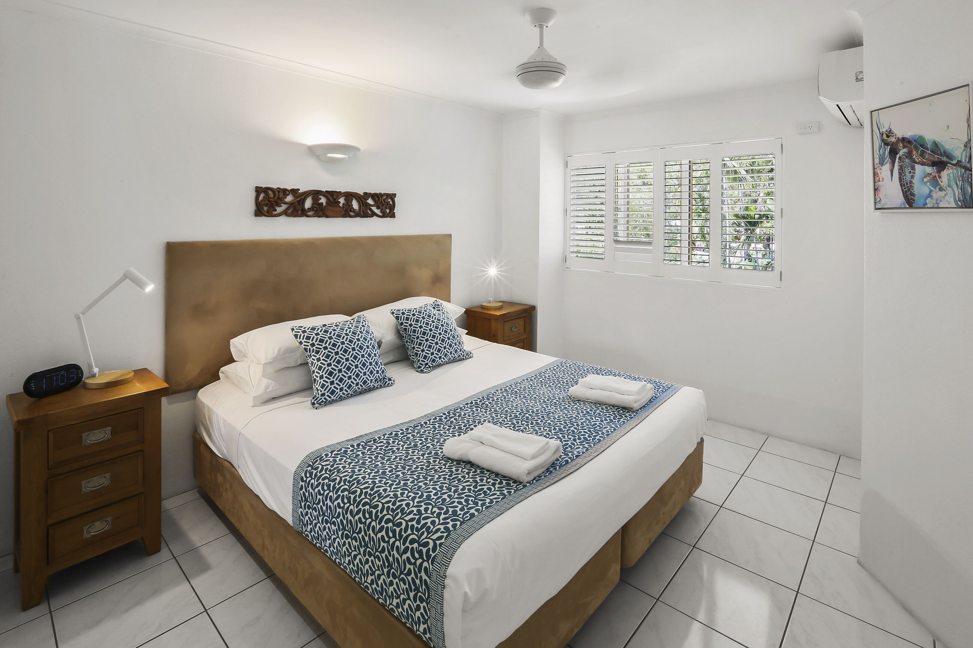 Una cama bien hecha con una colcha estampada, una lámpara de noche y una obra de arte en la pared.