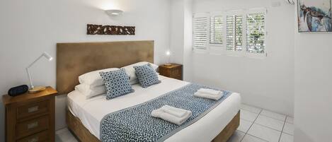 Una cama bien hecha con una colcha estampada, una lámpara de noche y una obra de arte en la pared.