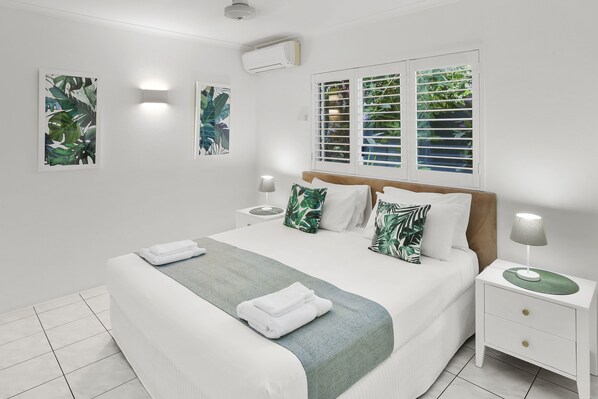 A neatly made bed with a green throw, white pillows, and a nightstand with a lamp. - Agincourt Beachfront Apartments (Clifton Beach)