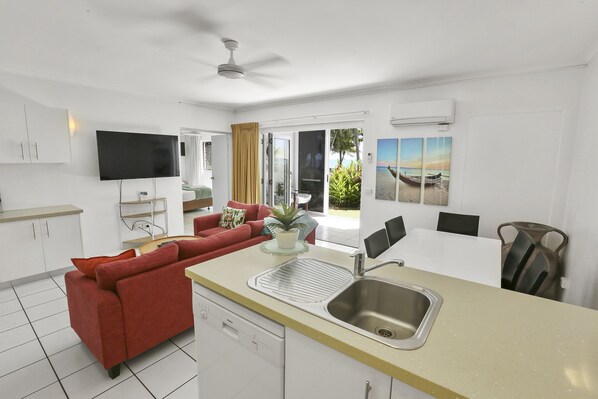 Una cocina moderna con una isla central, un comedor y una sala de estar con un sofá rojo.