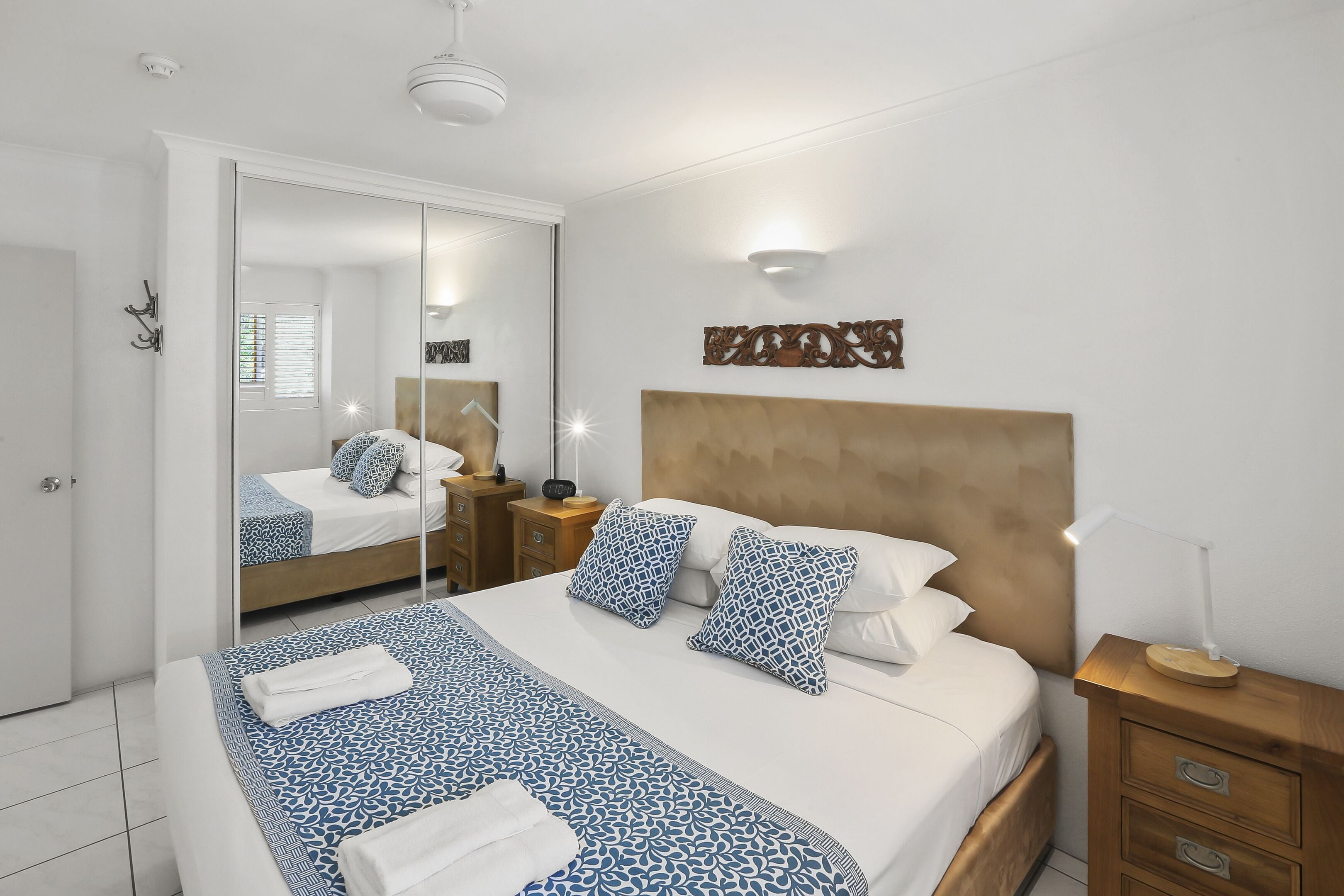 Un dormitorio ordenado con una cama grande, una mesita de noche, un espejo y una lámpara de pared.