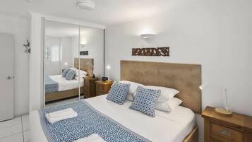 Une chambre à coucher bien aménagée, avec un grand lit, une table de chevet, un miroir et un luminaire fixé au mur.