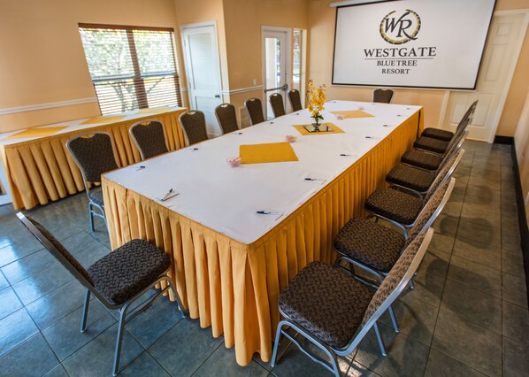 Un salón de conferencias con una larga mesa, sillas y una pantalla de proyector mostrando el logotipo del Westgate Blue Tree Resort.