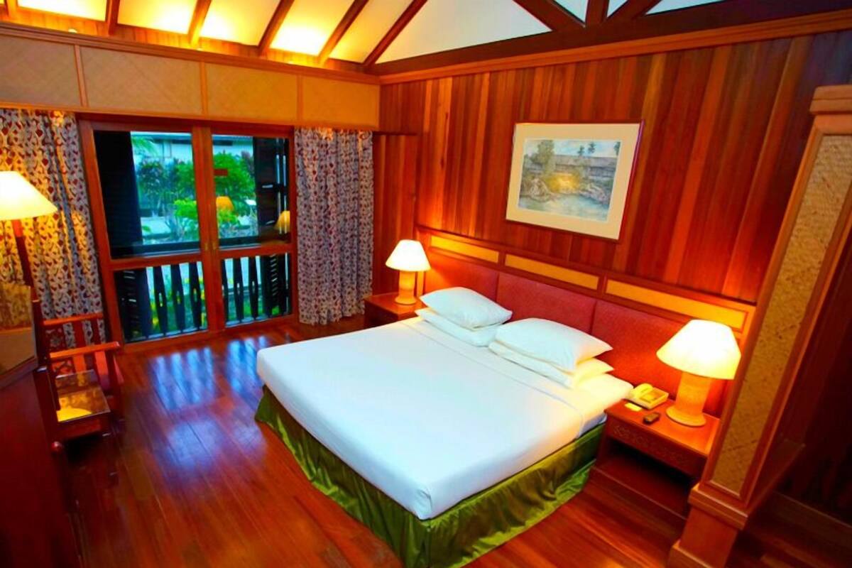 Habitación de hotel con una cama grande, paneles de madera, dos lámparas de noche, una ventana con cortinas y un cuadro enmarcado en la pared.