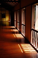 Corredor com piso de madeira e corrimão, que leva a um quarto com porta deslizante.