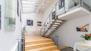 Un interior moderno con una escalera, barandillas de cristal y obras de arte en las paredes.
