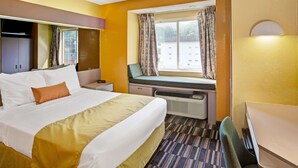 Habitación de hotel con cama, escritorio, silla, ventana con cortinas y calefactor.